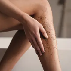 Kobieta wykonuje peeling kawowy na nogach, przygotowując skórę przed goleniem.