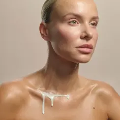 Kobieta z błyszczącą skórą, na której spływa biała substancja, przypominająca naturalny sebum.