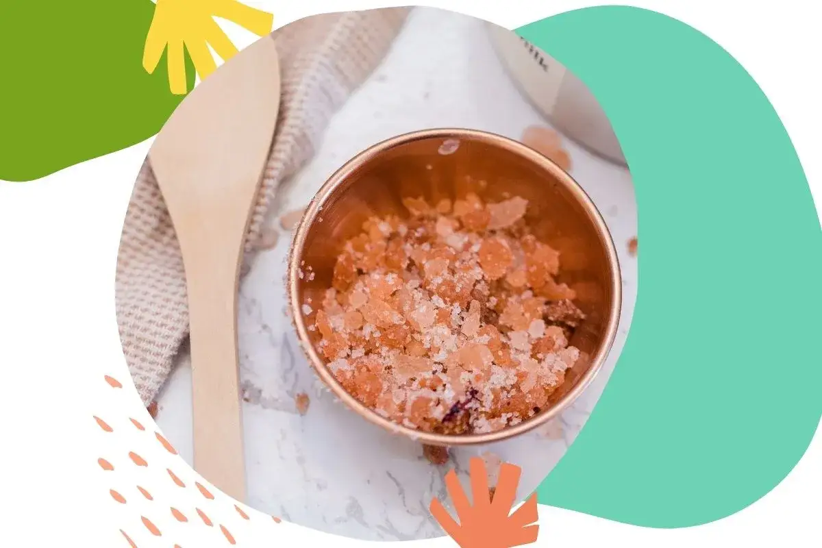 Miedziana miseczka z różowym, domowy peeling do twarzy. Obok drewniana łyżka i ręcznik.